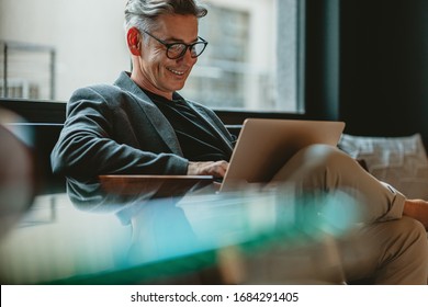Homem de negócios sorridente sentado no saguão do escritório, trabalhando em seu laptop. Profissional do sexo masculino trabalhando no saguão do escritório.