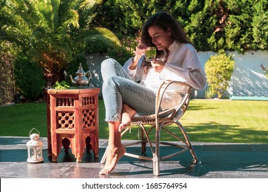 Mujer marroquí bebiendo té árabe tradicional en casa. Cultura y tradiciones árabes. Estilo de vida musulmán. Mujer joven árabe con rasgos étnicos que huele té árabe de menta en su jardín.