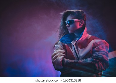 Stilvolles und futuristisches junges Model posiert in leuchtenden Neon-Studiolichtern mit Neon-Textprojektion auf rosa Hintergrund, trägt Rennblazer und holografische Sonnenbrille, umgeben von Rauch. Cyberpunk