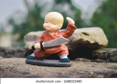 Cute sweet plastic Doll standing with sword and king costume on skateboard dress as wonder prince in action adventure. Close up portrait. Outdoor childhood fun play leisure game toddler background.