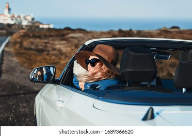 Retrato de moda de estilo de vida al aire libre de una mujer bastante joven conduciendo cabriolet. Chica feliz sonriendo, sosteniendo el sombrero, mirando la carretera. Con elegante abrigo de jeans, sombrero, gafas de sol. Mujer conduciendo. Viajar en automóvil