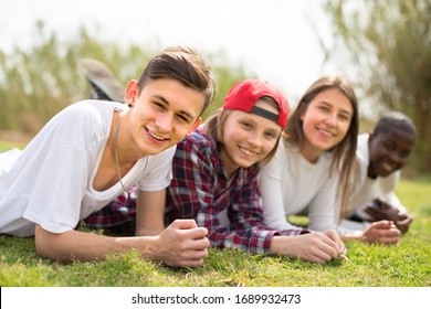 group of multinational modern teens lie in the park on the grass