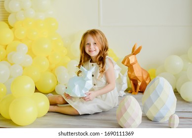 Lächelndes Ingwermädchen im weißen Kleid, das gemaltes Papierei hält. Bunter Hase. Glückliche Momente, gelber Ballonhintergrund. Hübsches Kind. Oster- und Feiertagskonzept