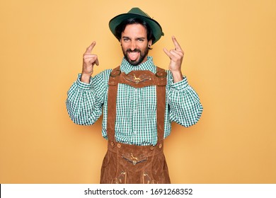 Young handsome man wearing tratidional german octoberfest custome for Germany festival shouting with crazy expression doing rock symbol with hands up. Music star. Heavy music concept.