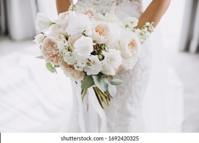 una joven con un vestido de novia blanco sostiene en sus manos un ramo de flores y vegetación con una cinta