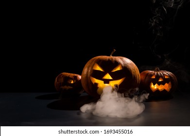 Halloween kaart. jack o lantern met kaarsen gloeien op een zwarte achtergrond. Een rij enge pompoenen met uitgesneden grimassen rookt in het donker.