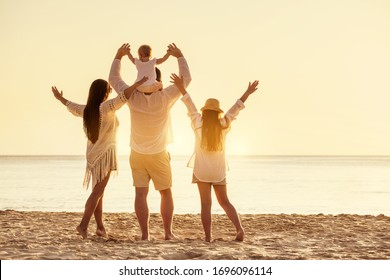 Familia feliz de cuatro pueblos está de pie con los brazos levantados en la playa del mar al atardecer