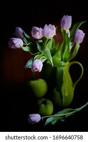 Un ramo de tulipanes lilas en un frasco verde con manzanas verdes cubiertas de gotas de lluvia sobre fondo negro