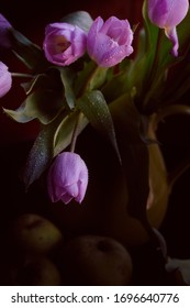 Một bó hoa tulip màu hoa cà trong lọ màu xanh lá cây với những quả táo xanh phủ đầy những hạt mưa trên nền đen