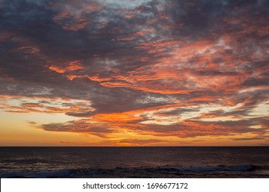 Zeegezichtsamenstelling van een zonsondergang, donkergrijze oceaan, lage horizon, verlicht met heldere rode en oranje wolken na zonsondergang. Donkere humeurige lucht met roze en oranje wolken.