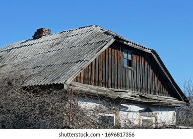 old brown wooden attic of a rural house with a small window under a gray slate roof against a blue sky