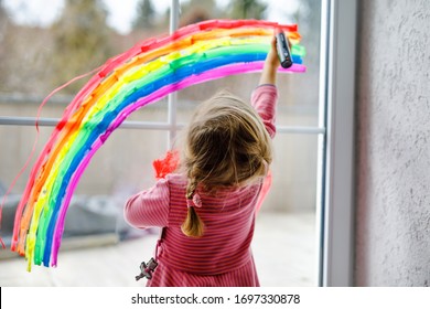 Adoralbe niña pequeña con arco iris pintado con un colorido color de ventana durante la cuarentena del coronavirus pandémico. Niño pintando arcoíris alrededor del mundo con las palabras Vamos a estar todos bien.