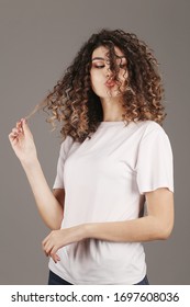 
Portrait of a happy young woman standing.Sexy woman in a white t-shirt on a gray background. Beautiful girl T-shirt design with afro curly and beautiful hair. Emotions.Mock-Up