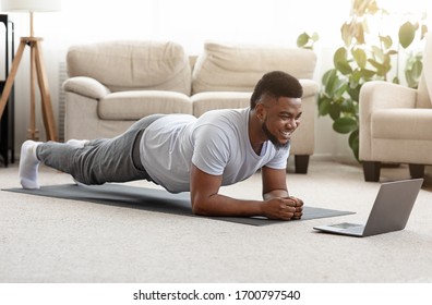 自宅でのトレーニング。ラップトップでオンライン チュートリアルを見ながらヨガの板をしているスポーティな男、リビング ルーム、空きスペースで運動