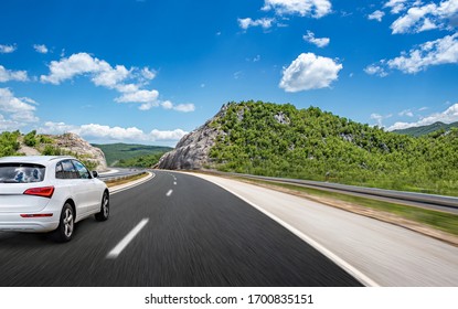 Witte auto beweegt op de weg tussen de bergen en bossen. Gemengde media.