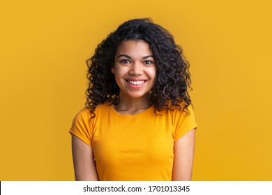 明るい背景に若い魅力的なアフリカ系アメリカ人女性の肖像画。彼女の顔に広い完璧な笑顔で幸せそうに見えるボリュームのある巻き毛を持つかわいい女の子。
