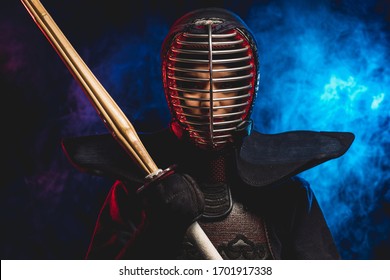 retrato de luchador de kendo en uniforme y casco protector. guerrero de combate sosteniendo shinai en la mano espada de bambú aislado sobre espacio ahumado