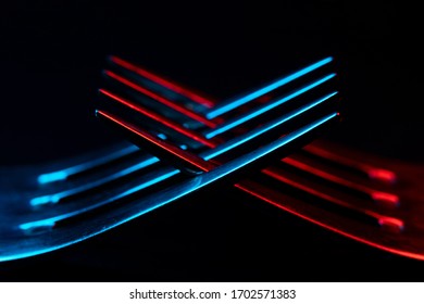 Close-up of prongs of a dining fork, illuminated in red and blue. Abstract object, isolated against a black background. Selective focus with bokeh.