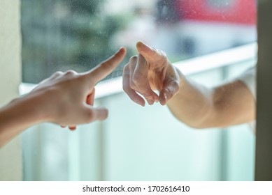 Manos separadas por una ventana de vidrio para el distanciamiento social durante el bloqueo del virus de la corona