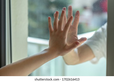 Manos separadas por una ventana de vidrio para el distanciamiento social durante el bloqueo del virus de la corona