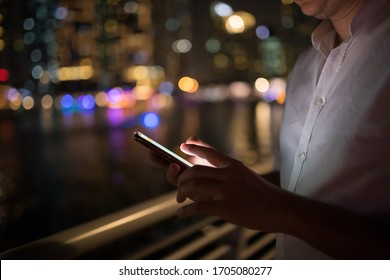 Imagen de primer plano de manos masculinas usando un smartphone por la noche en la calle comercial de la ciudad. Concepto de búsqueda o redes sociales