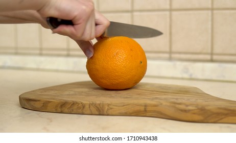 Woman cuts an orange in half. Woman's hand close up