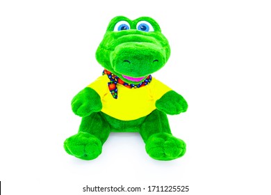 Peluche suave, verde, juguete de cocodrilo para niños aislado en un fondo blanco con reflejo de sombra. Vista frontal. La hermosa muñeca está vestida con una camiseta amarilla y una bufanda colorida.