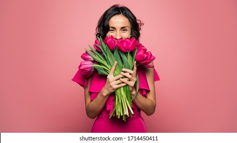 Internationale Vrouwendag. Uiterst gelukkige vrouw in een felroze jurk ruikt een bos lentebloemen, die ze in haar handen houdt.