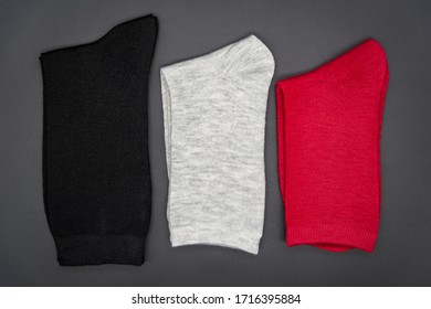 Drei Paar Socken grau schwarz rot liegen gefaltet auf einem schwarzen Hintergrund