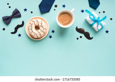 Happy Fathers Day flat lay on blue, copy space. Morning coffee, donut, gift box with confetti and moustache, Father's Day celebration concept.