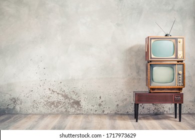 Retro classic old analog TV receivers set and aged wooden television stand with outdated amplifier front aged concrete wall background. Broadcasting, news concept. Vintage style filtered photo