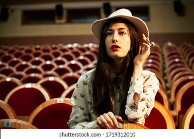 Retrato de una linda chica hipster en una sala de cine con sombrero, soñando sola, concepto de gente de moda y estilo de vida