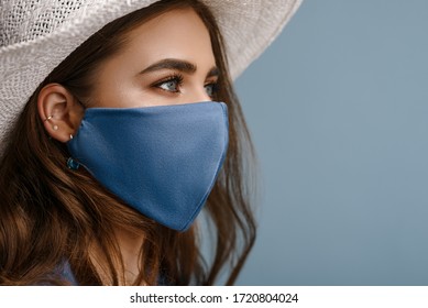 Mujer con elegante mascarilla protectora, posando sobre fondo azul. Accesorio de moda de moda durante la cuarentena de la pandemia del coronavirus. Cierra el retrato de estudio. Copiar, espacio vacío para texto