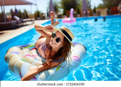 Cô gái trẻ tươi cười mặc bikini, đội mũ rơm thư giãn trên con thiên nga bơm hơi trong bể bơi. Người phụ nữ hấp dẫn trong bộ đồ bơi nằm dưới ánh nắng mặt trời trong kỳ nghỉ nhiệt đới. Nữ sinh xinh xắn tắm nắng tại resort cao cấp.