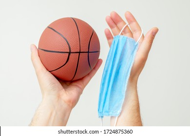 Manos de hombre sosteniendo una pelota de baloncesto con máscara protectora médica sobre fondo claro durante el coronavirus. Baloncesto en pausa por coronavirus.