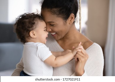Nahaufnahme einer glücklichen jungen afroamerikanischen Mutter, die ein kleines Kind oder Kleinkind umarmt, eine liebevoll lächelnde, biraciale Mutter umarmt, ein kleines Babykind umarmt, einen zärtlichen Familienmoment genießt, Mutterschaft, Kinderbetreuungskonzept