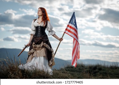 Girl in historical dress of 18th century with flag of United States. July 4 is US Independence Day. Woman of patriot freedom fighter in outdoor on background cloudy sky
