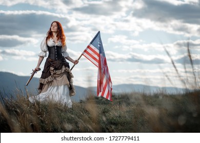 Girl in historical dress of 18th century with flag of United States. July 4 is US Independence Day. Woman of patriot freedom fighter in outdoor on background cloudy sky