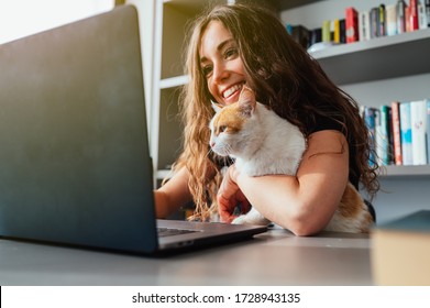 Gelukkige jonge kaukasische vrouw met haar kat die laptop thuis met behulp van. Slim werken en slim studeren met huisdier