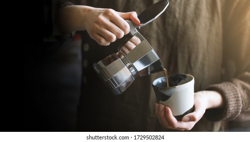 Barista menuangkan kopi dari pembuat kopi moka pot ke cangkir kopi kecil. Pembuatan kopi profesional. Latar belakang kabur.