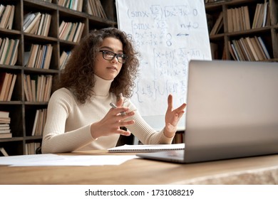 Female young hispanic school math teacher, college tutor coach looking at webcam and talking in classroom giving virtual teaching remote class online lesson by zoom conference call on laptop computer.