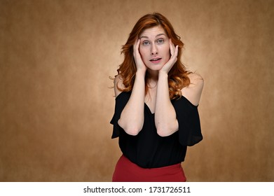 Studiofoto einer hübschen kaukasischen jungen Frau in einer schwarzen Bluse mit langen roten Haaren auf beigem Hintergrund. Model-Schauspielerin zeigt verschiedene Emotionen, während sie vor der Kamera spricht.