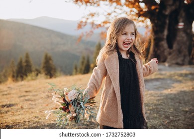 日没時に秋の山に立ち、花束を手に持つ、小さくてスタイリッシュな美しいモデルの女の子のポートレート