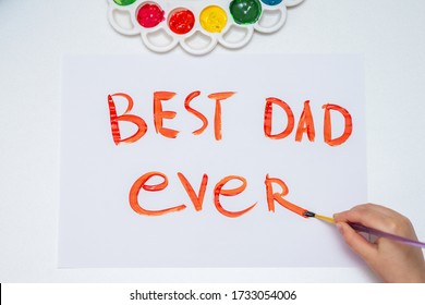 Vue vun uewen op eng Zeechnung vun enger Hand vun engem Kand, déi handgeschriwwenen Text "Best Dad Ever" op wäissem Pabeier weist. Konzept vum Alles Guddes zum Pappendag.