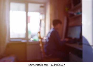 A man is sitting at a table and working at a computer at home in self-isolation mode early in the morning at dawn, the concept of lack of time and deadline, the bokeh and blur effect