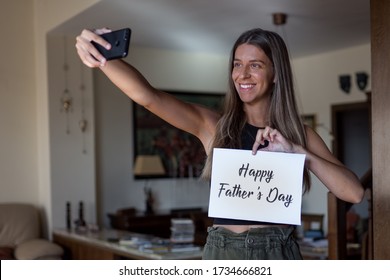 Cô gái tóc vàng mỉm cười và làm facetime cho Ngày của Cha trong COVID-19. Cô ấy đang cầm một tấm thiệp có dòng chữ 'Chúc mừng Ngày của Cha'
