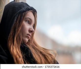 窓の近くで休んでいる黒いパーカーを着たローアングルの悲しい十代の少女