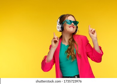 Enjoy listening to music. Young redhead woman in headphones listening music. Funny smiling girl in earphones and pink jacket dancing and singing on yellow background. Relaxation and stress management.