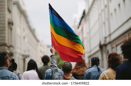 Tampilan belakang orang-orang dalam parade kebanggaan. Sekelompok orang di jalan kota dengan bendera pelangi gay.