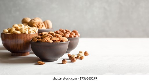 Hazelnut, kacang mete, almond, dan kenari. Kacang dalam mangkuk kayu dan tanah liat dengan latar belakang abu-abu dengan ruang fotokopi. Spanduk.